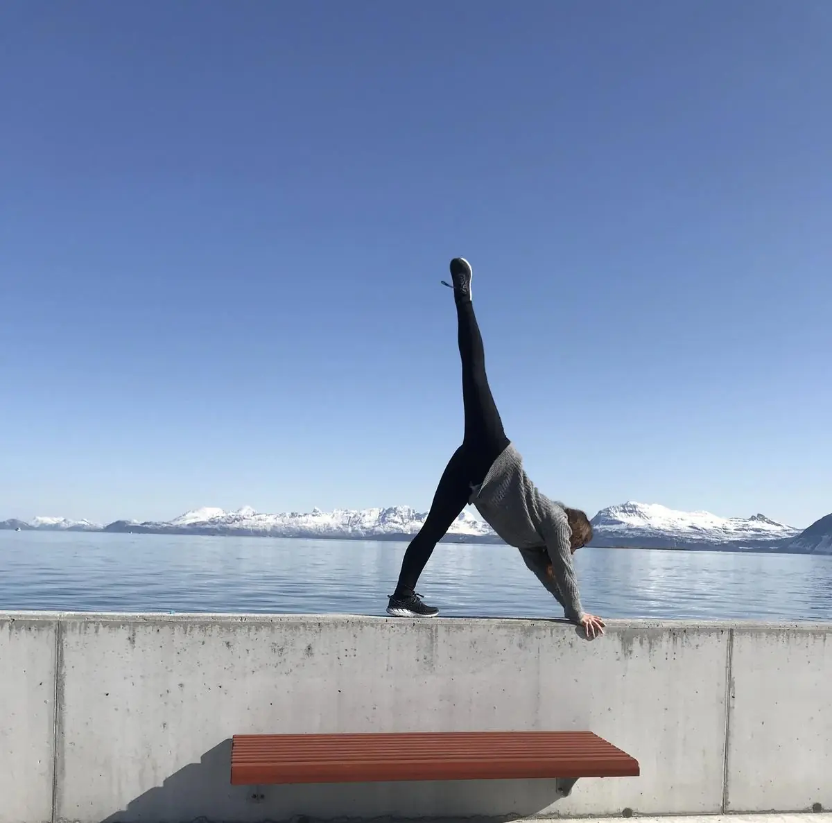 Sara i trekantstilling på en kai med fjell og fjord bak